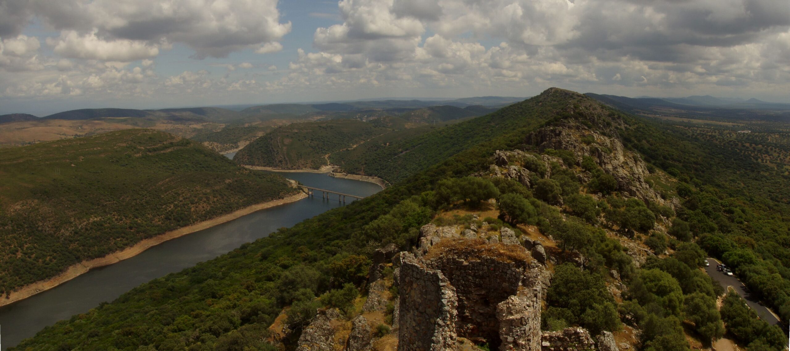 Castillo_Monfrague_4 Dos visitantes observan y fotografían el paisaje rocoso de Monfragüe desde una pasarela de madera junto al río.